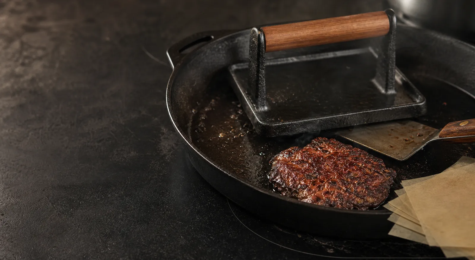 Heavy cast-iron burger press beside a hot skillet