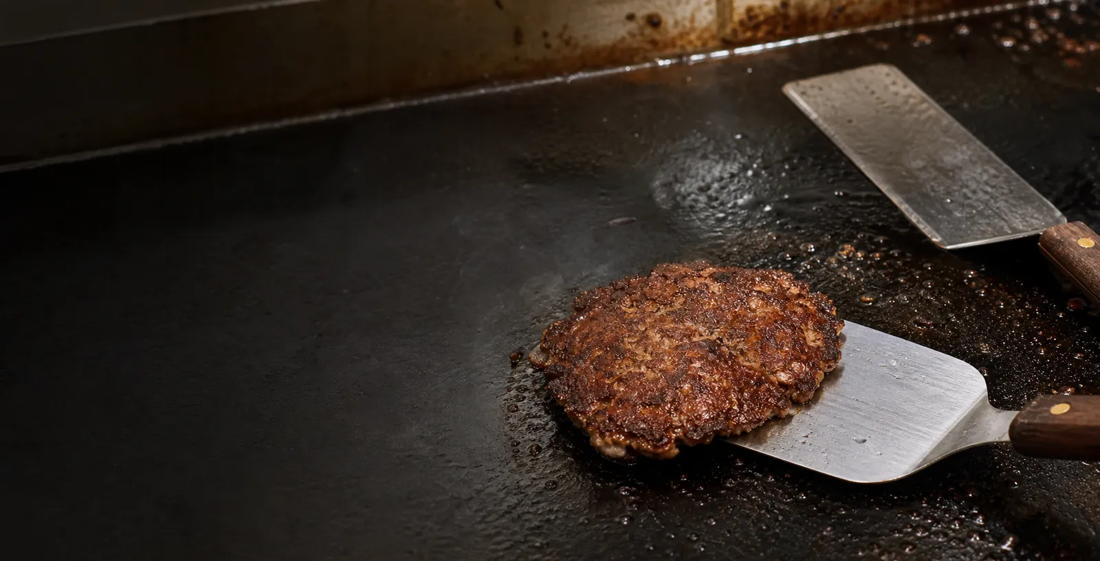 A crisp smash burger patty being lifted from a griddle