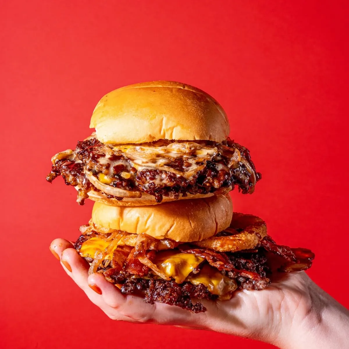 Stacked smashburgers held against a red background at Wanna Smash