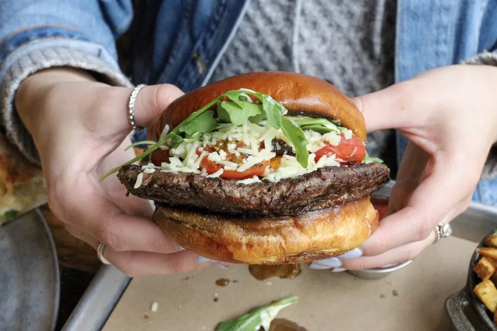 Parlor Pizza Bar burger with tomato, arugula, cheese, and brioche bun