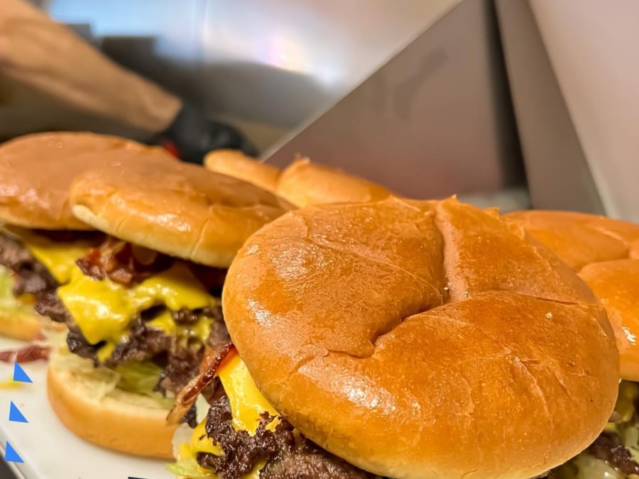 Flat-top griddle at Sid's Diner with onion burgers pressing — onions caramelizing into patties
