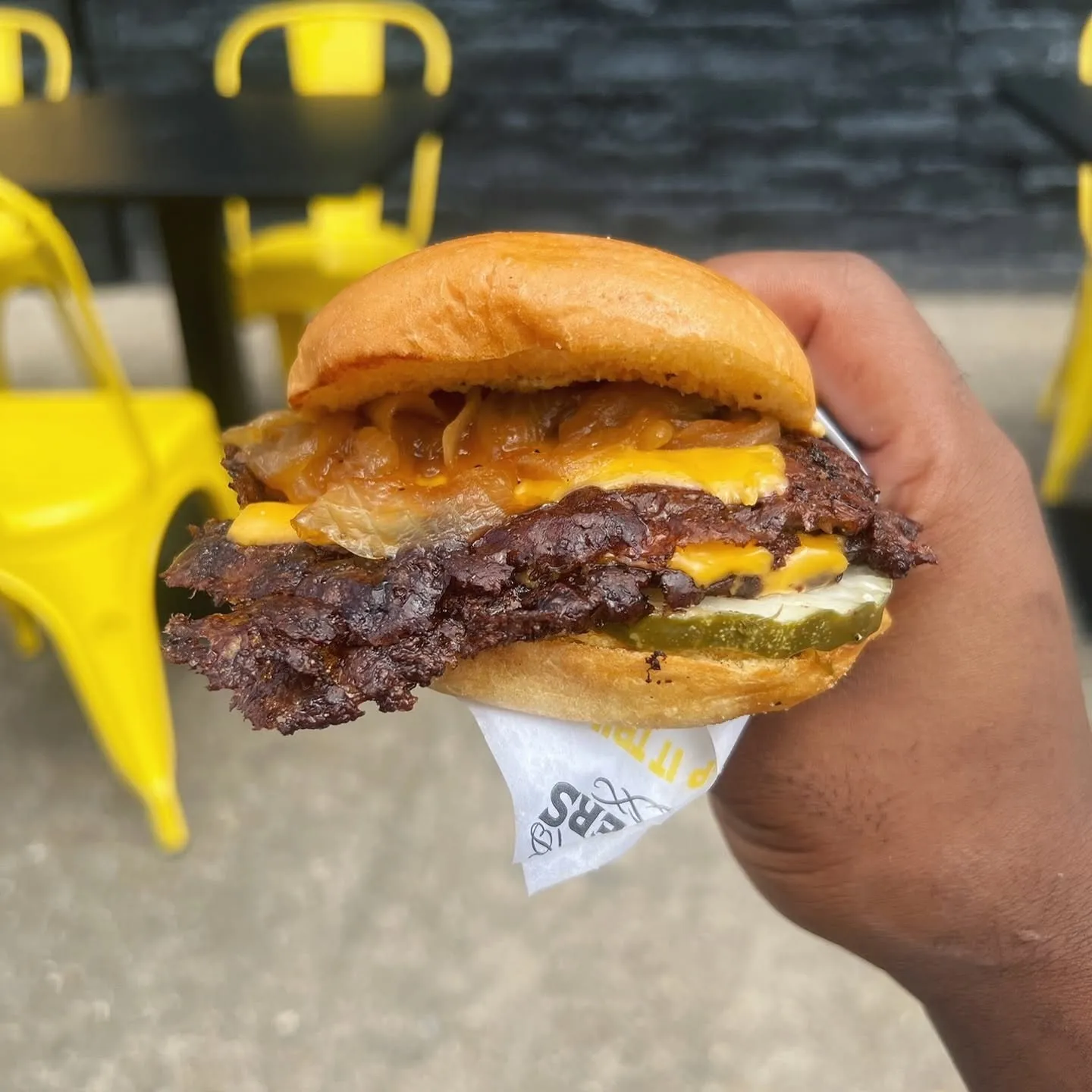 Close-up of a Trill Burgers double smashburger with crispy beef edges, cheese, onions, and pickles